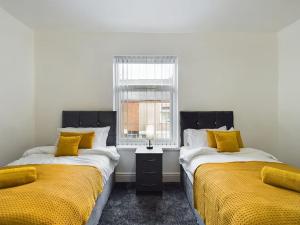 2 camas en una habitación con sábanas amarillas y ventana en Cliff House By RMR Accommodations - NEW - Sleeps 8 - Modern - Parking, en Stoke on Trent