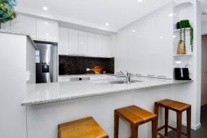 a kitchen with white cabinets and a sink and two stools at Stunning Ground Floor City Apartment 104 in Cairns