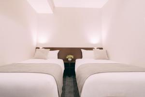 two beds in a room with white walls at R Hotel Honmachi in Osaka