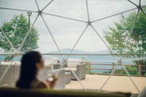 a woman sitting at a table looking out of a window at LUONTE 霧の高原 Glamping 