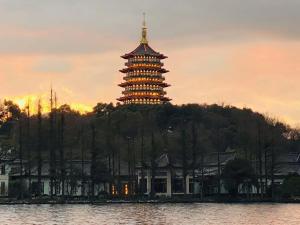 a pagoda on top of a hill next to a lake at West Lake Hefang Street Metro Exit B&B in Hangzhou