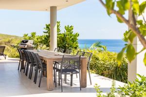 - une table et des chaises en bois sur une terrasse donnant sur l'océan dans l'établissement Luxury 12-Person Villa in Cas Abou with Pool, Seaview, and Private Beach Access, à Willibrordus