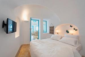 1 dormitorio con cama blanca y TV en la pared en Ananda Suites, en Imerovigli
