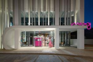 Una mujer con un vestido rosa caminando delante de un edificio en Moxy Lisboa Oriente en Lisboa