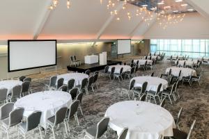 ハダーズフィールドにあるCedar Court Hotel Huddersfieldの白いテーブルと椅子、スクリーンが備わる会議室