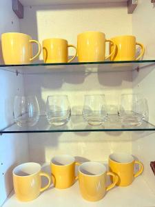 une rangée de tasses et de verres jaunes sur des étagères dans l'établissement 2-bedroom Flat in Sydenham, à Forest Hill