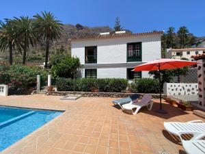 una casa con piscina, sombrilla roja y sillas en Apartamento Nelly A3, en Valle Gran Rey