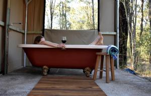 Una donna sdraiata in una vasca da bagno con un bicchiere di vino di On Bell Glamping a Belford