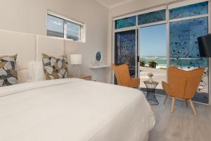 a white bedroom with a large bed and two chairs at Absolute Ocean Boutique Guesthouse in Hermanus