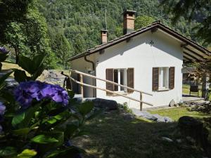 uma pequena casa branca num jardim com flores roxas em Verzasca: Casa Sonia em Frasco