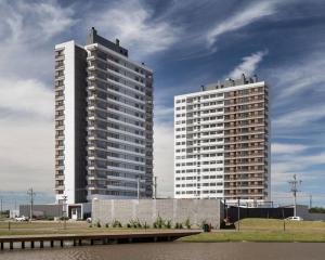 two tall white buildings next to a body of water at Apartamento pura vida no Parque Una com vaga de garagem. in Pelotas