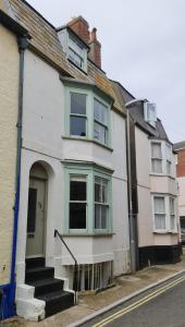 a white house with green windows on a street at Blue Ensign Cottage in Weymouth