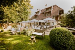 un jardin avec des chaises et des tables en face d'une maison dans l'établissement La Pinte du Vieux Manoir, à Morat