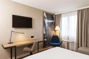 ein Hotelzimmer mit einem Bett und einem TV an der Wand in der Unterkunft NH München Airport in Oberding