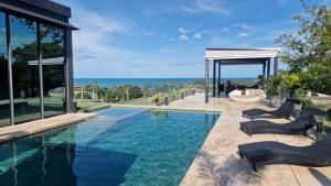 a swimming pool with chairs and the ocean in the background at Villa Obsidian, with staff, sea view and walk to Choeng Mon beach in Choeng Mon Beach
