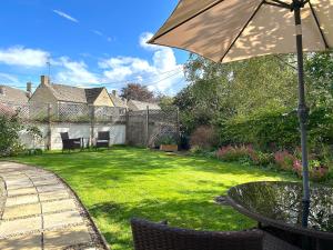 a patio with a table and an umbrella in a yard at Cosy Cotswold Cottage with garden Quenington near Bibury in Quenington