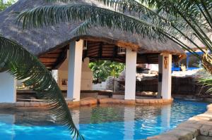 a resort swimming pool with a thatch roof at Sandriver Resort in Musina