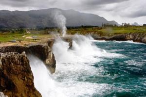 a waterfall on the side of a cliff next to the water at vivienda vacacional la tejavana in Llames de Pría