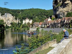 un homme assis sur un mur près d'une rivière avec un bateau dans l'établissement Gîte Chez Pierrot - La vallée des châteaux, à La Roque-Gageac