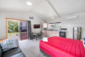 a bedroom with a red bed and a kitchen at Jack & Di's Lakefront Motel in Rotorua