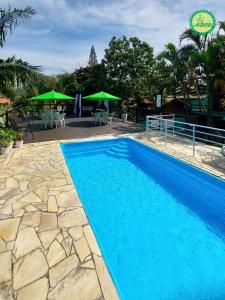 a blue swimming pool with tables and green umbrellas at Pousada Arthemis in Garopaba