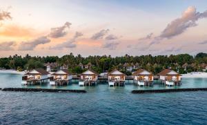 Une rangée de bungalows sur pilotis sur l'eau au coucher du soleil dans l'établissement Bandos Maldives, à Atoll Malé Nord