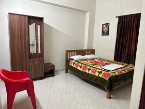 um quarto com uma cama e uma cadeira vermelha em Jothi Residency em Madurai