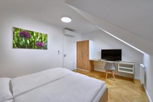 a white bedroom with a bed and a desk with a television at DownTown Suites Rubesova in Prague