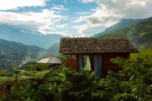 uma pequena casa numa colina com montanhas ao fundo em O'chau Homestay Sapa em Lao Cai