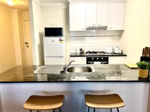 eine Küche mit weißen Schränken, einer Spüle und 2 Stühlen in der Unterkunft ReadySet Apartments on Kavanagh in Melbourne