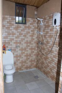 e bagno con doccia e servizi igienici in un muro di mattoni. di Munyana homestay a Rwinkwavu