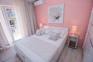 a bedroom with a white bed and a pink wall at APARTMAN KSENIJA KOVAČIĆ in Stanići