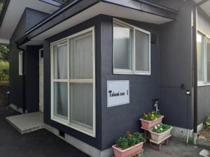 une maison noire avec deux fenêtres et deux plantes en pot dans l'établissement Takumisou1, à Kiso-fukushima