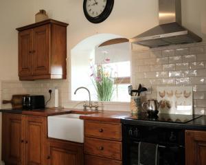 eine Küche mit einem Waschbecken und einer Uhr an der Wand in der Unterkunft Drumnavaddy Cottage in Dromore