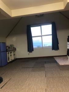 Cette chambre mansardée dispose d'une grande fenêtre avec des rideaux bleus. dans l'établissement Guest House Kizuna, à Oshamambe