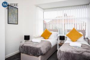 1 dormitorio con 2 camas con almohadas amarillas y ventana en Stylish 3 bedroom property Newcastle, en Kenton