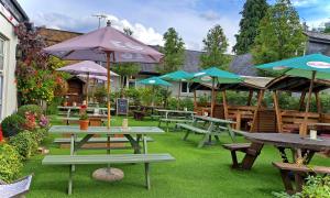 The Inn West End في ووكينغ: مجموعة من طاولات النزهة مع مظلات على العشب