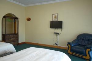 a bedroom with a bed and a chair and a tv at Unique Bed and Breakfast in Harare