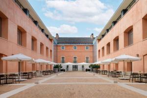 an empty courtyard of a building with tables and umbrellas at NH Collection Palacio de Aranjuez in Aranjuez