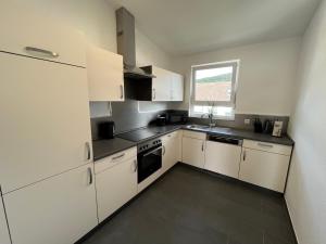 una pequeña cocina con armarios blancos y una ventana en Premium Apartment 70qm 2 Zimmer Küche, Balkon, Smart TV, WiFi en Aalen