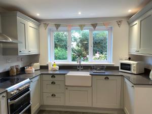 a kitchen with white cabinets and a sink and two windows at Charming country cottage in quiet rural setting 