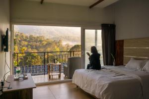 uma mulher sentada numa cama num quarto com uma grande janela em Munnar Majestic Resorts by VOYE HOMES em Anachal