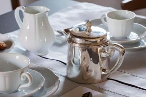 eine silberne Teekanne auf einem Tisch mit Tassen und Untertassen in der Unterkunft Dimora Cottanera in Castiglione di Sicilia
