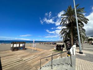 a sandy beach with a palm tree and a boardwalk at Casa Sami in Playa de las Americas