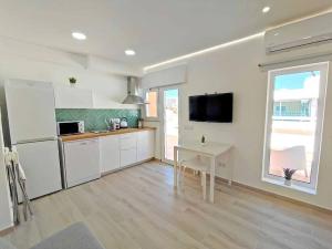 a kitchen with white cabinets and a table and a tv at Lovely Terrace Studio Baixa Faro in Faro