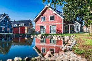 ein großes rotes Haus mit einem Teich davor in der Unterkunft Ferienhäuser Baltic Lagoon Haus 14 in Fuhlendorf