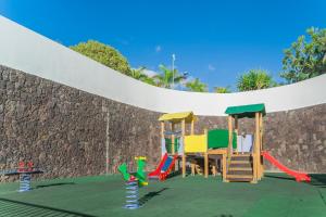 a playground with colorful play equipment in front of a stone wall at Sunset Harbour Club in Adeje