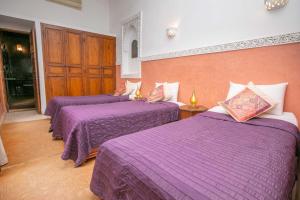 three beds in a room with purple sheets at Riad Marélia in Marrakesh