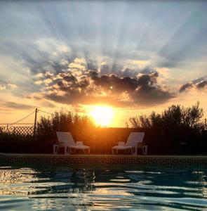 a sunset with two chairs next to a swimming pool at Terre Villa Katia in Santa Maria di Licodia