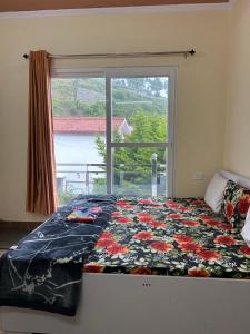 a bed in a room with a window with a floweridered blanket at Host Labs Homestay - Premium View - Close to Kaichi Dham, Bhimtal, Sattal, and more in Bhīm Tāl